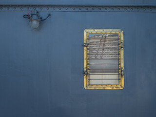 The metal wall of the ship is dark gray-blue with a porthole and a lantern. A square porthole in a...