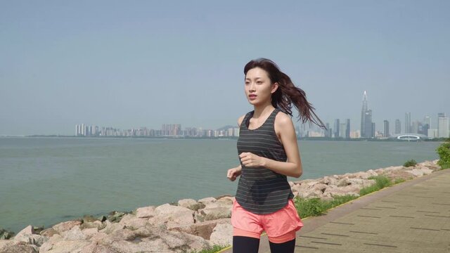 young asian woman jogging exercising in a seaside park in modern city