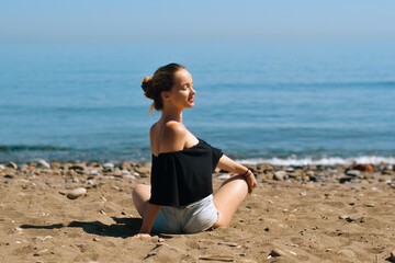 Fototapeta na wymiar A beautiful girl is engaged in yoga on the beach against the background of the sea. Health and sports. A woman on the ocean shore meditates and relaxes. Summer and travel.
