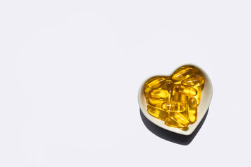 Capsules with fish oil in a plate in the shape of a heart on a white background. Top view, place for text.