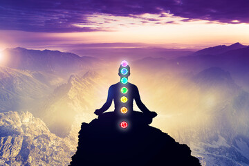 Meditating men in yoga lotus position with seven chakras. Mindfulness and self awereness practice. Silhiuette of meditation on mountains backgraound landscape