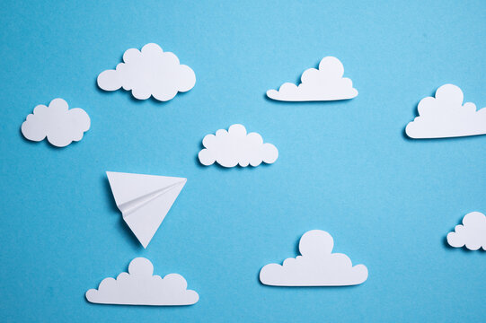 Papierflieger fliegt durch aus Papier ausgeschnittene Wolken und blauen Himmel
