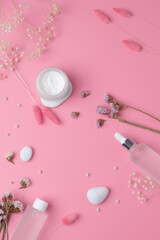 Cosmetic skin care products with flowers on pink background. Flat lay.