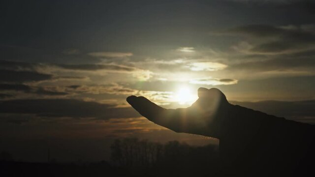 Silhouette of one hand holding the sun, opening, revealing the sun