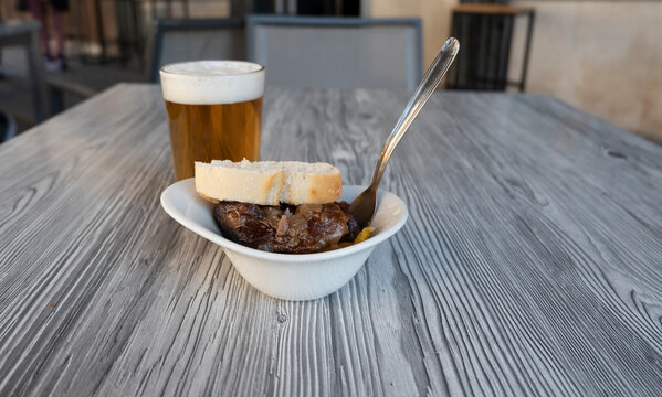 Close-up photo of a fresh beer in a glass and an aperitif of pork cheeks on the terrace of a Spanish bar.
