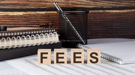 Fototapeta premium FEES text on the wooden block with notebooks on the chart