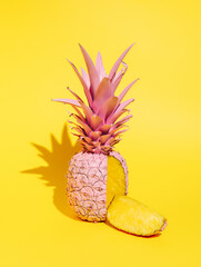 Pink pineapple with a cut slice isolated on a bright yellow background. Creative food concept. Tropical summer fruit composition. Pop art aesthetic.