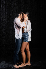 romantic young adult wet couple standing in rain and sensually hugging with hands on black background