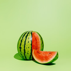 A whole ripe and juicy watermelon with a cut slice isolated on a light green background. Minimal summer fruit concept. Pop art food design.