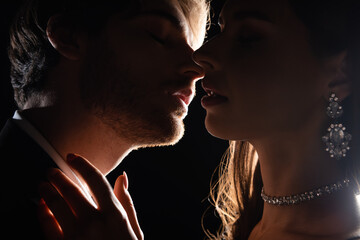 close up view of attractive elegant couple gently kissing in back light isolated on black