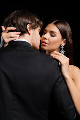 seductive woman gently hugging elegant man in black blazer and white shirt isolated on black
