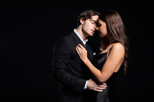 elegant young adult man and woman hugging and kissing isolated on black
