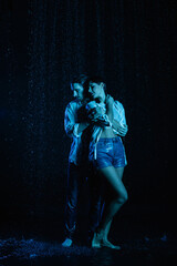 good-looking man gently hugging wet sensual woman in water drops on black background with blue color filter
