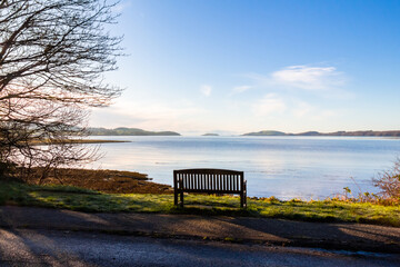 An empty wooden seat or bench over looking the sea at Kirkcudbright Bay