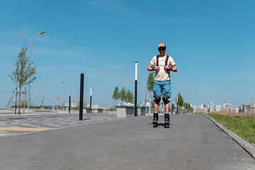 Obraz premium young man in blue shorts and cap, in protective equipment riding on roller skates on the asphalt road in summer, roller blading