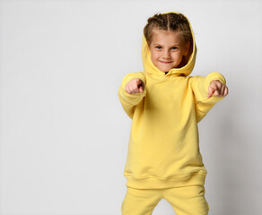 Beautiful little schoolgirl, pointing to the tebf, wearing a new tracksuit. Cute baby posing in a stylish yellow tracksuit on a white background. Stylish sportswear concept.