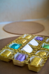 wrapped luxury chocolates in various colours for different flavours in a golden container on a brown background.