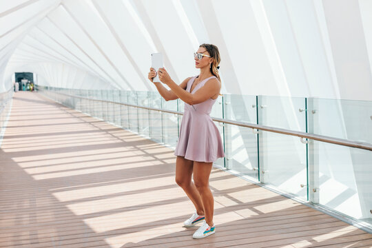 A young woman in a summer dress walks and takes a photo on a tablet
