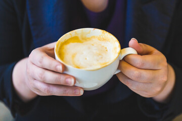 A cup of coffee cuppuccino in female hands.