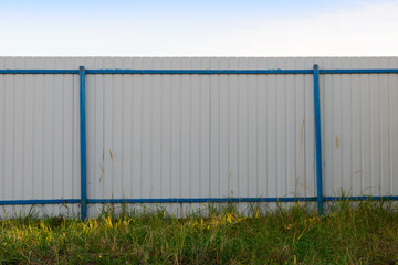 Obraz premium Grey metal perforated fence with blue posts in a green clearing