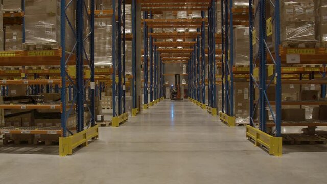 Distant forklift turning around corner in long corridor of logistical warehouse