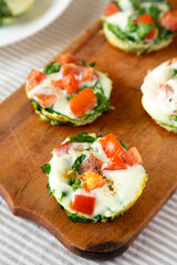 Homemade Egg White Breakfast Cups with Spinach and Tomato on a rustic wooden board, side view.