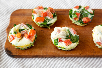 Homemade Egg White Breakfast Cups with Spinach and Tomato on a rustic wooden board, low angle view.