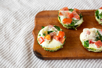 Homemade Egg White Breakfast Cups with Spinach and Tomato on a rustic wooden board, low angle view. Copy space.