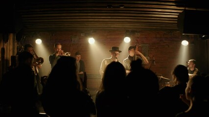 DOLLY OUT CU to WIDE People dancing during concert of a modern jazz band playing on a stage of a small crowded venue. Shot with 2x anamorphic lens - Powered by Adobe