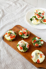 Homemade Egg White Breakfast Cups with Spinach and Tomato on a white wooden background, side view.