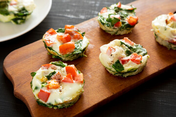 Homemade Egg White Breakfast Cups with Spinach and Tomato on a rustic wooden board on a black surface, side view.