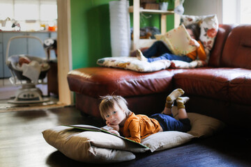 Obraz premium Funny children read books on soft mattresses on the couch and on the floor, real interior, dark style