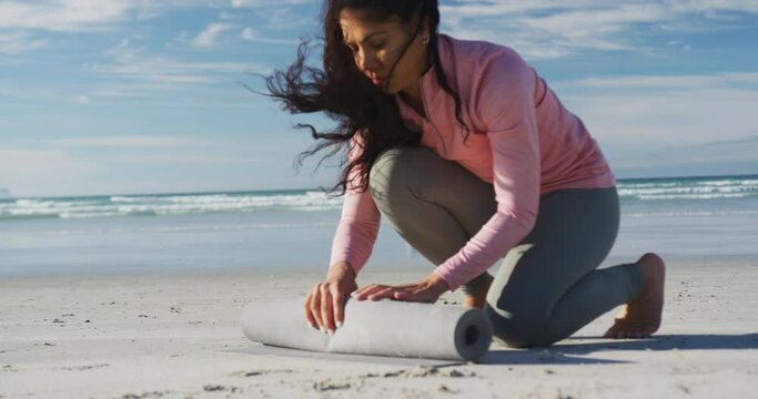 Mixed race woman rolling yoga mat at the beach