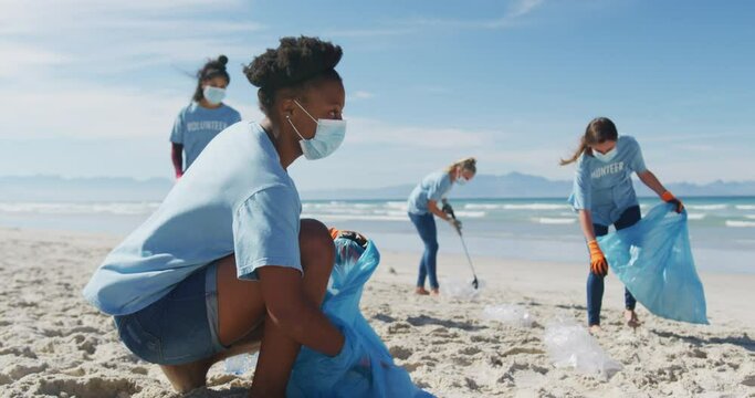 Diverse group of women wearing volunteer t shirts and face masks picking up rubbish from beach
