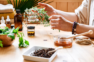 Woman prepares aromatherapy session at the table with essential oil diffuser medical herbs, different types of oils and essences. Aromatherapy and alternative medicine concept. Natural remedies.