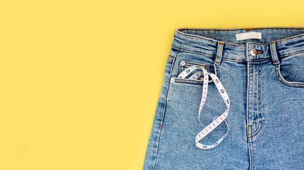 Measuring tape and jeans on a bright yellow background. Weight loss concept by summer