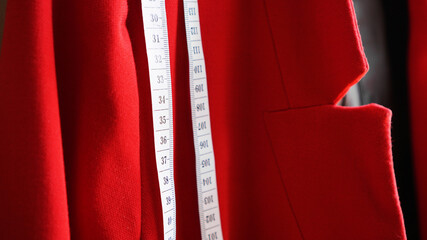 White measuring tape on the background of the red fabric of the jacket. Sewing clothes concept