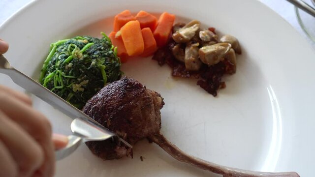 Knife and fork eating one rack of lamb with vegetable dish