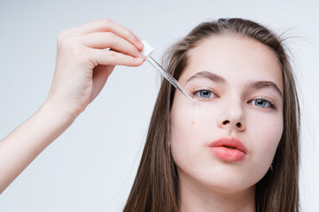 Close-up photo. Girl with long hair applies serum to the skin with a pipette looking at the camera