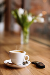 Cup of coffee, car remote key and vase of flowers on wooden table in coffee shop, selective focus. The concept of freelance. copy space