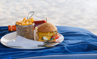 Classic beef burger with cheese and french fries. on white plate. Fast food on the beach. Blue background. Selective focus.