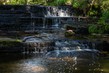 Cascading waterfall cascades in Estonia in green light at summertime