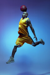 Handsome african-american male basketball player in action and motion in neon light on blue...