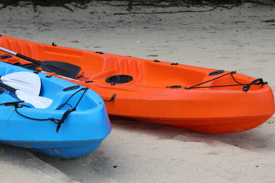 Two boats pair of empty free kayaks in red and blue with a paddle on the sand.Close-up