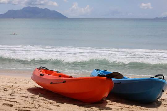Two red and blue kayaks on a sandy beach by the sea with an island on the horizon and a sky with white clouds on a warm summer day.Background image.Vacation and travel concept