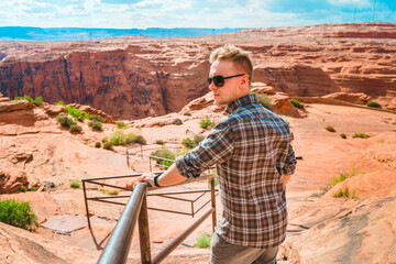 A young man walks down the red rocks to the observation deck on the Colorado River at sunset,...