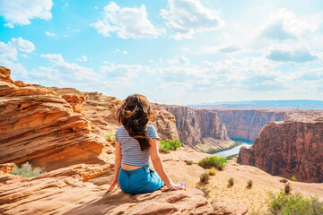 A young woman on red rocks admires the view of Glen Canyon Dam, Arizona