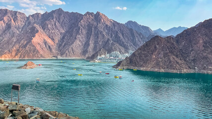 Hatta Dam Lake in mountains enclave region of Dubai, United Arab Emirates is famous tourist attraction with scenery and place to enjoy kayaking boat ride and other water adventure activities. - obrazy, fototapety, plakaty