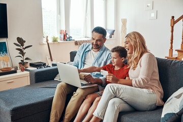 Young beautiful family shopping online and smiling while using laptop at home