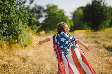 Happy little boy patriot running in the field with American flag